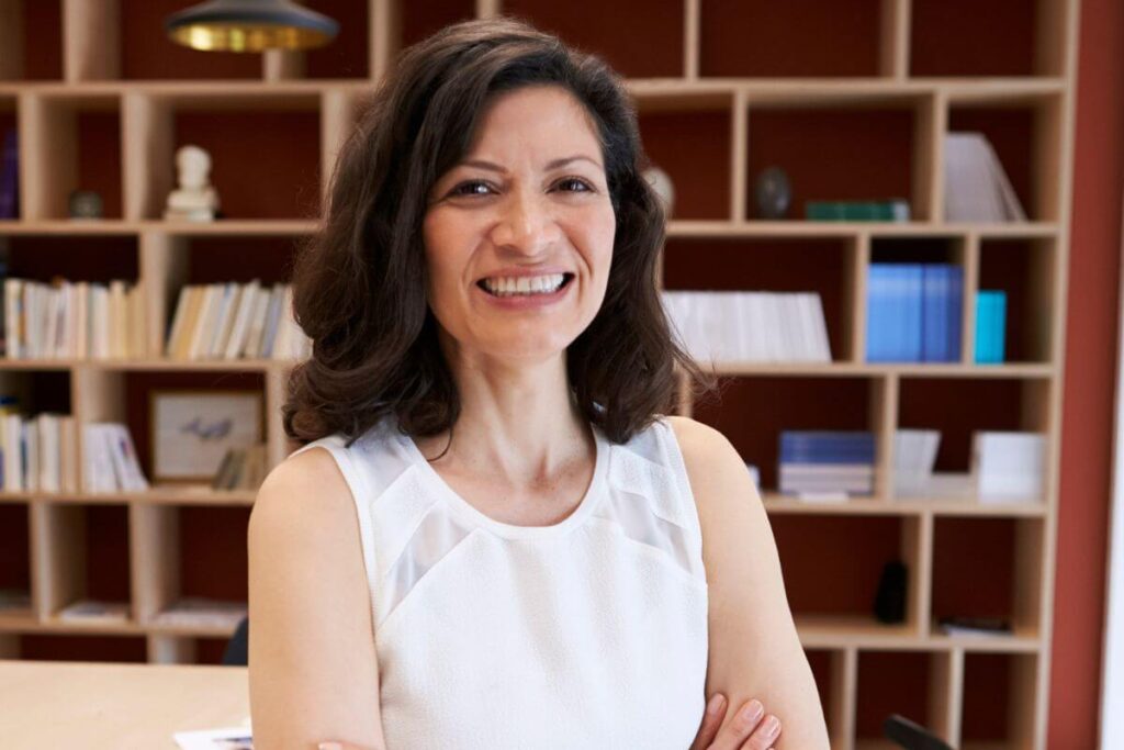 a beautiful confident middle aged woman with brown hair stands in front of library shelves and smiles at the camera because she has learned about 10 rules for success and happiness