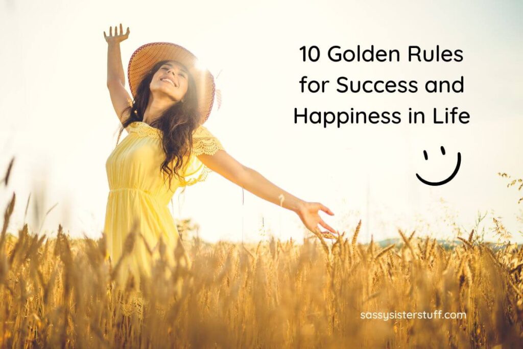 a young woman in a yellow dress straw hat stands in a wheat field with the sun gleaming behind her and her arms happily throw up in the air