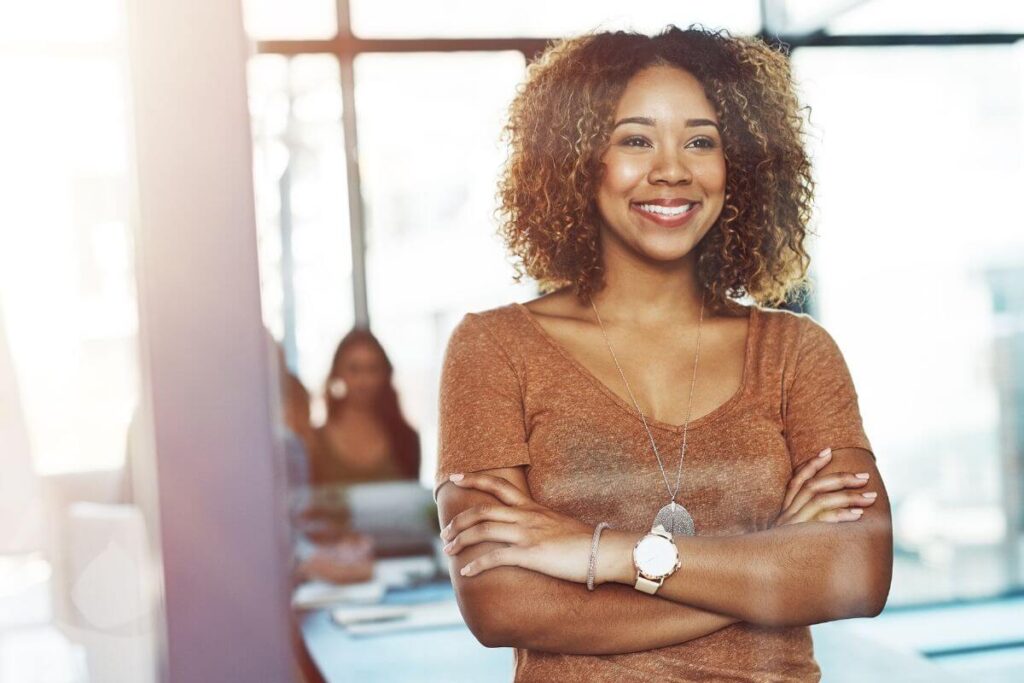 an African American young woman smiles confidently out a window from her office after reflecting on her affirmations for confidence and courage