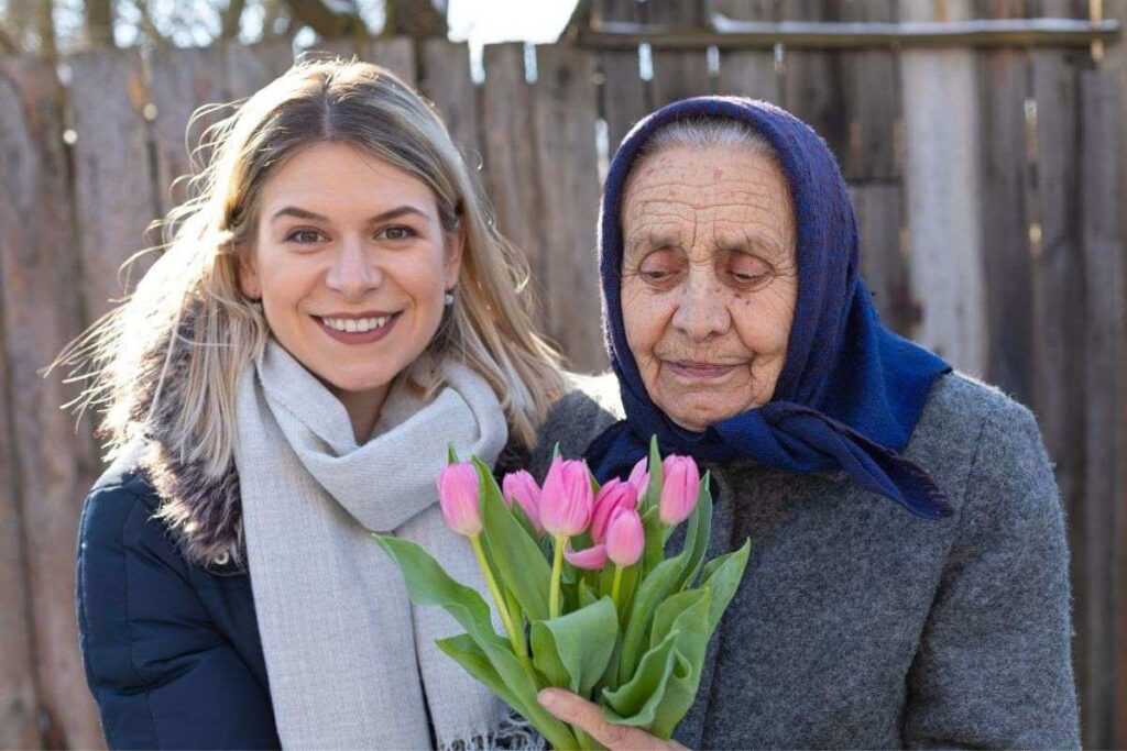 a young woman smiles with love and hugs her ailing grandmother