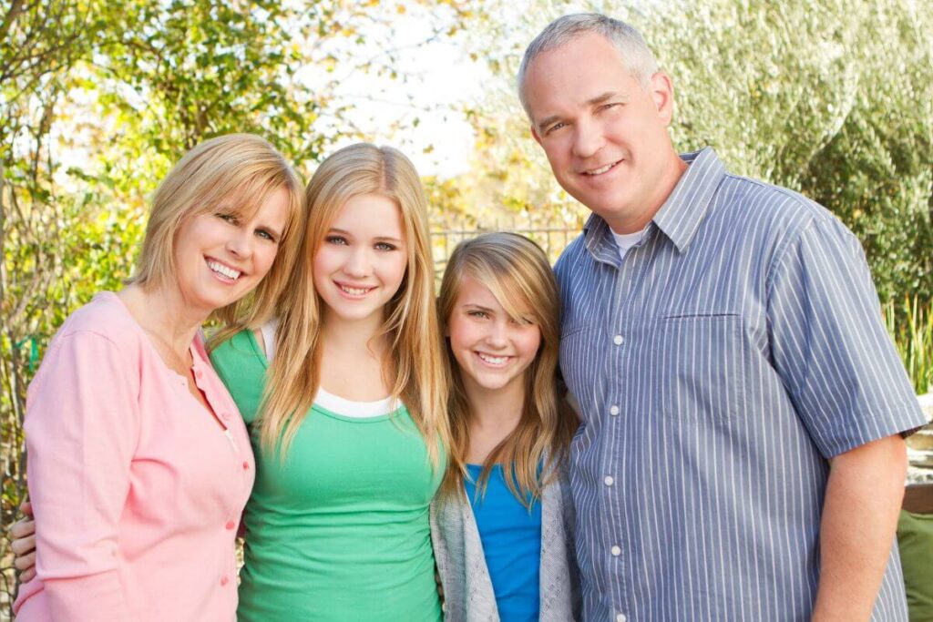 mom dad and two older teenage daughter pose for a family photo in the park