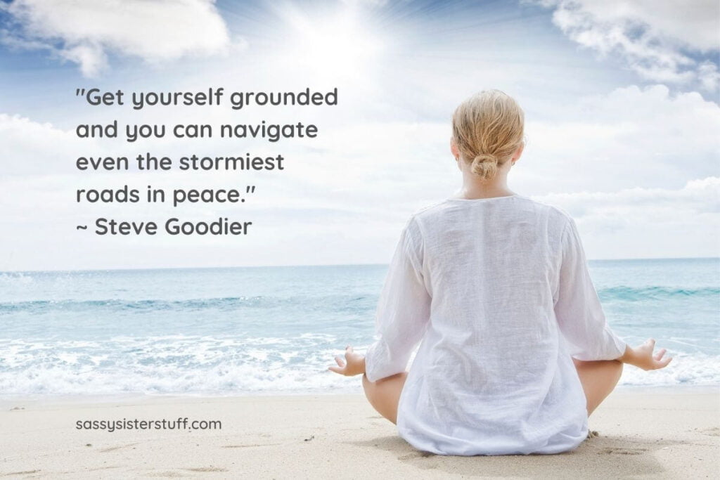a woman sits in the lotus yoga pose on the sand facing the ocean reciting her grounding affirmations plus a grounding quote