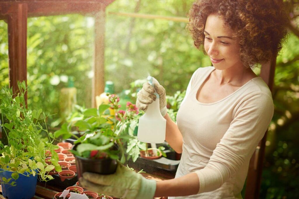 a happy woman demonstrates how to show up for yourself as she works in her green house watering the plants