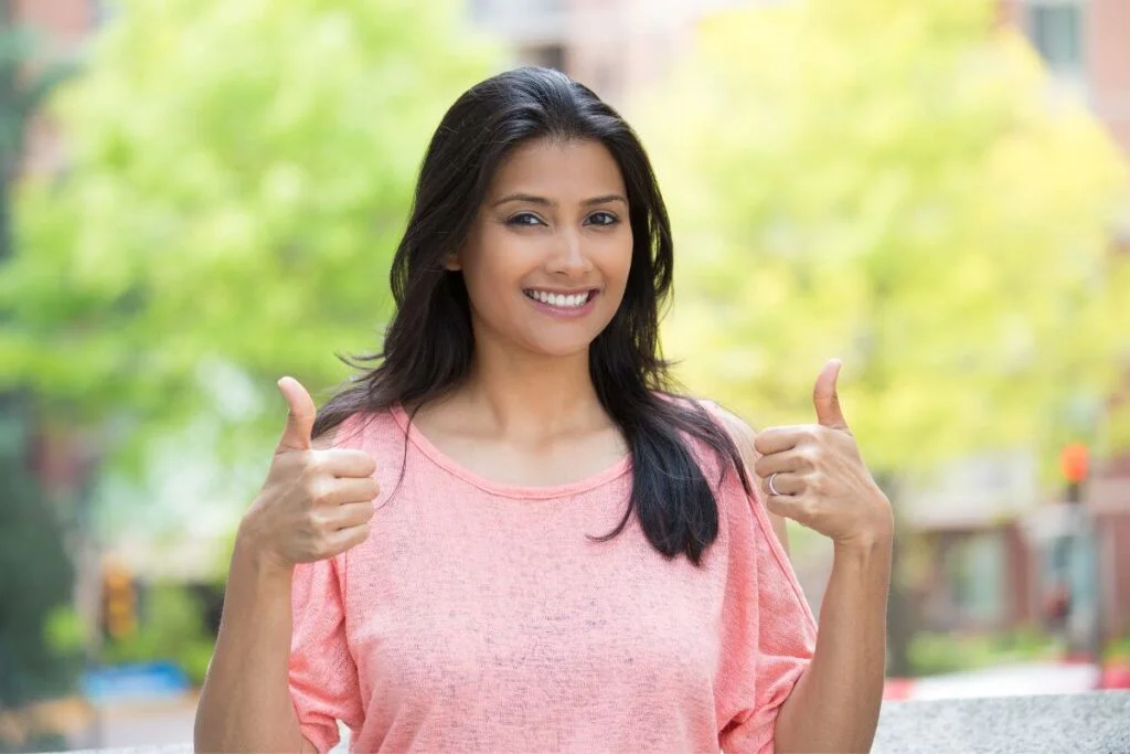 a happy young woman gives two thumbs up because she has learned how to show up for yourself