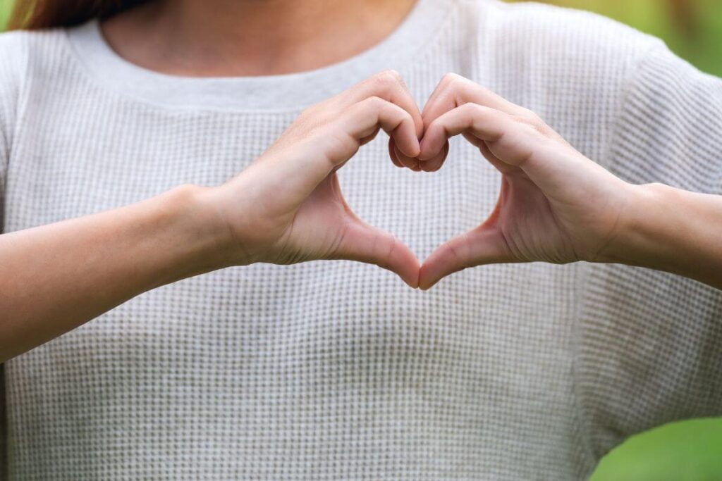 a close up of a female body wearing a simple white shire with hands making a heart in from of her chest