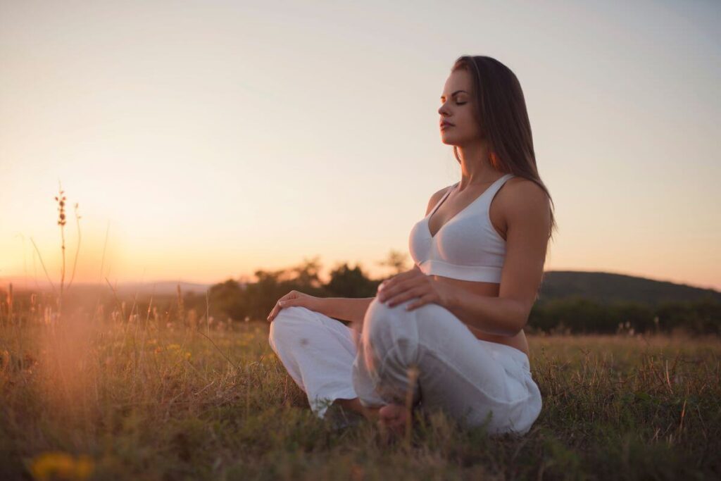 a young woman sits in a field of grass doing yoga and mindfulness affirmations