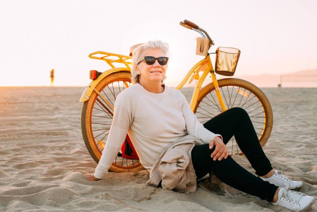 a middle aged woman rests against her old fashioned bike on a beach and reflects on her life well lived