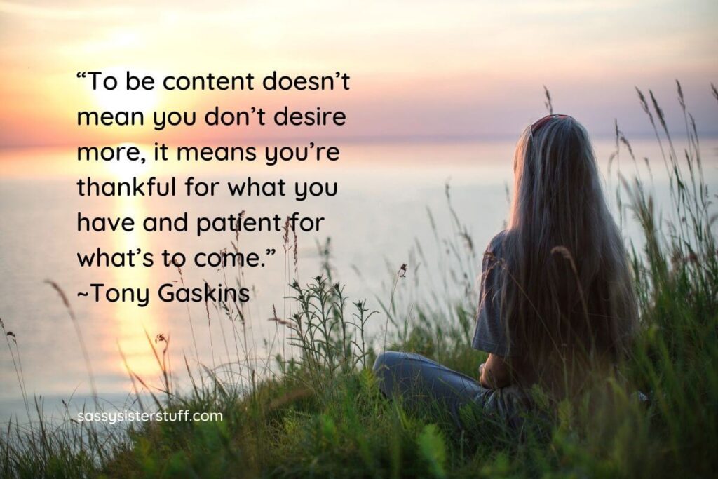 a woman sits in water grass and looks out over a lake as she thinks about the meaning of being happy and content plus a quote about how to be content