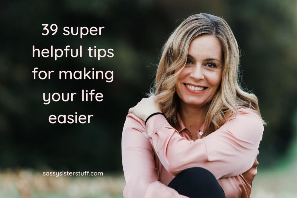 happy woman smiles at the camera as she sits in the grass of a park for a cover image of 39 super helpful tips for making your life easier