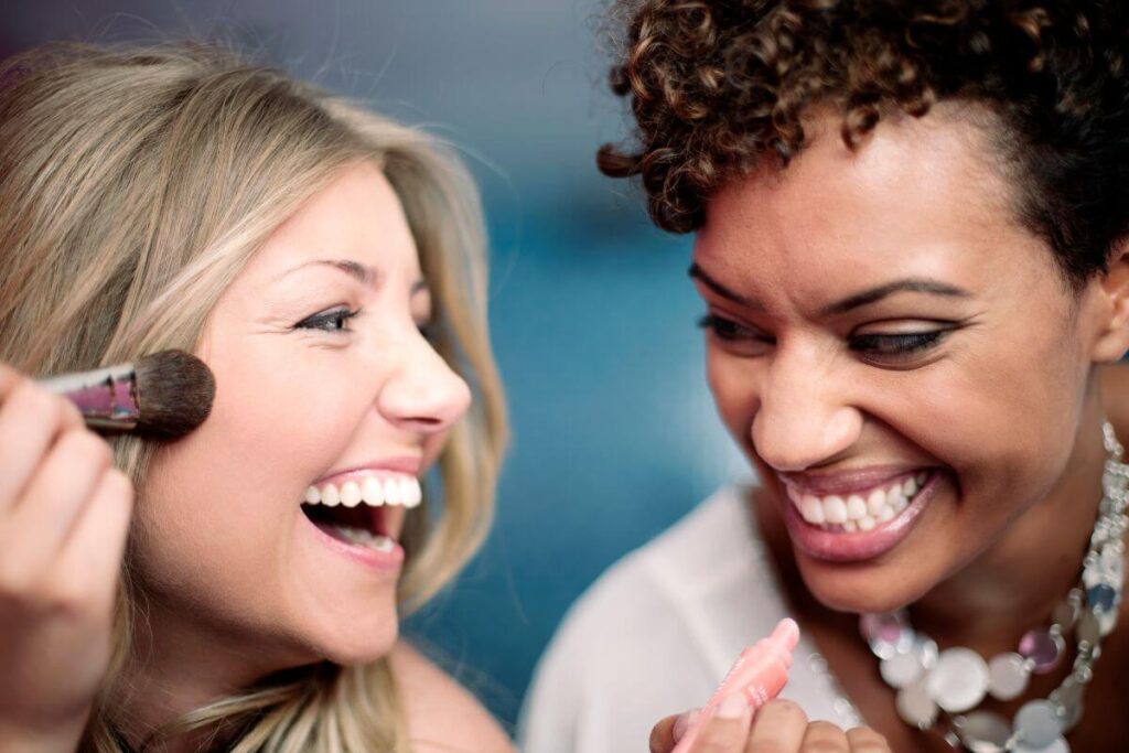 two women laugh together as they put finishing touches on their make up