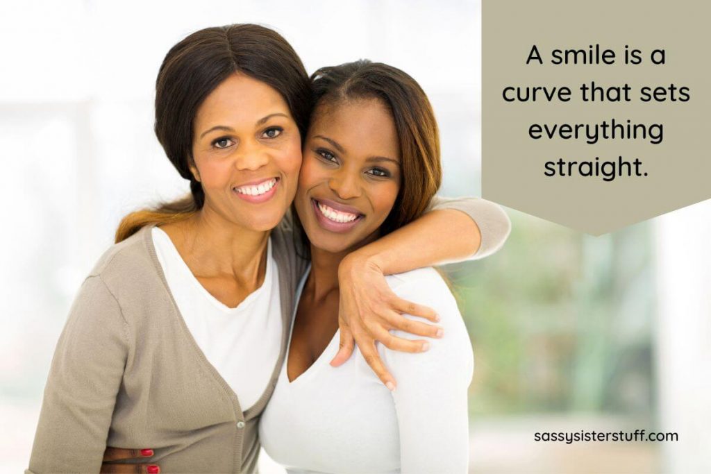 two dark skinned beautiful women embrace cheek to cheek and smile because they know a smile sets everything straight