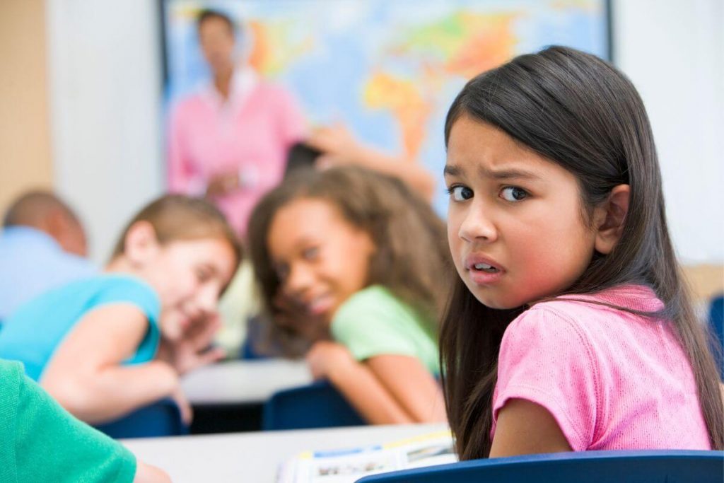 a young girl in a classroom is bullied by other girls sitting near her