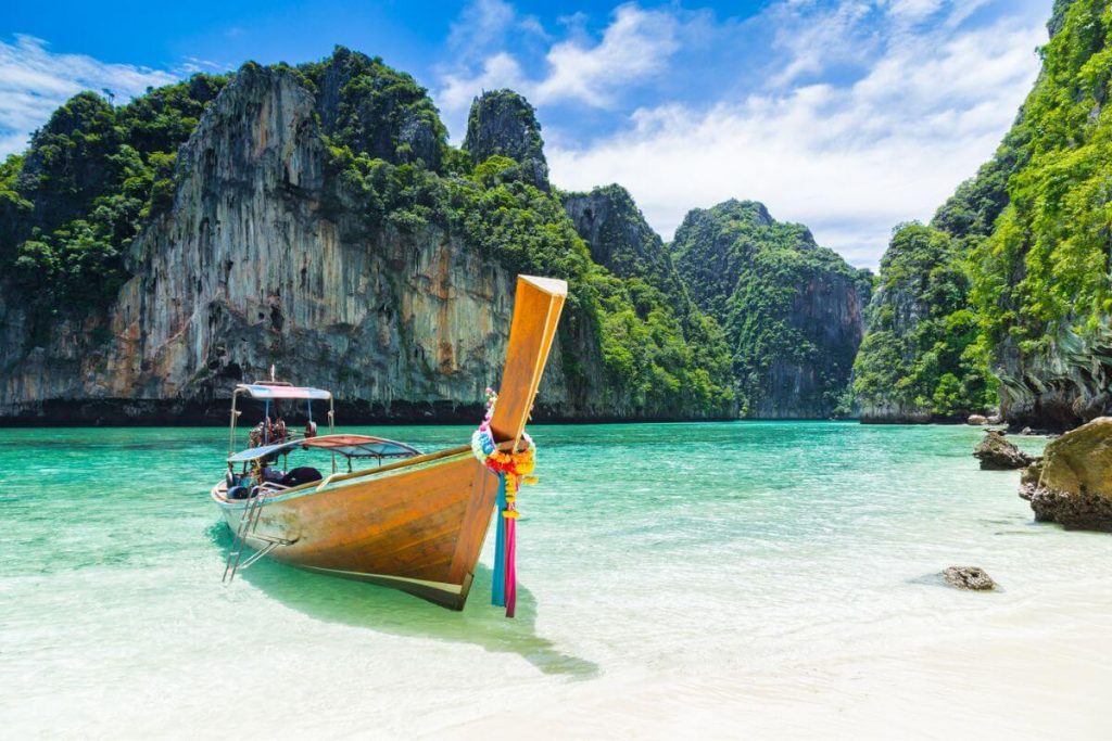a small boat sits on the shoreline of a beautiful beach surrounded by tall rock formations