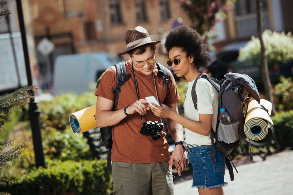 a young backpacking couple looks at a phone for directions as they travel in a foreign city