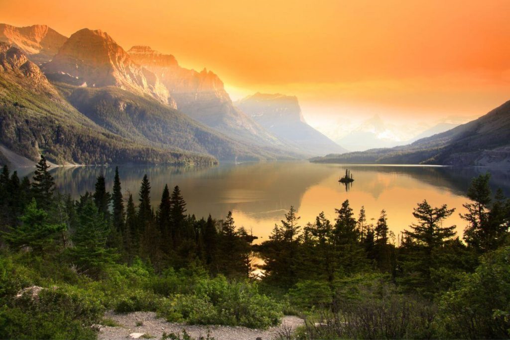 a beautiful orange sky surrounds mountains a large lake and beautiful ever greens