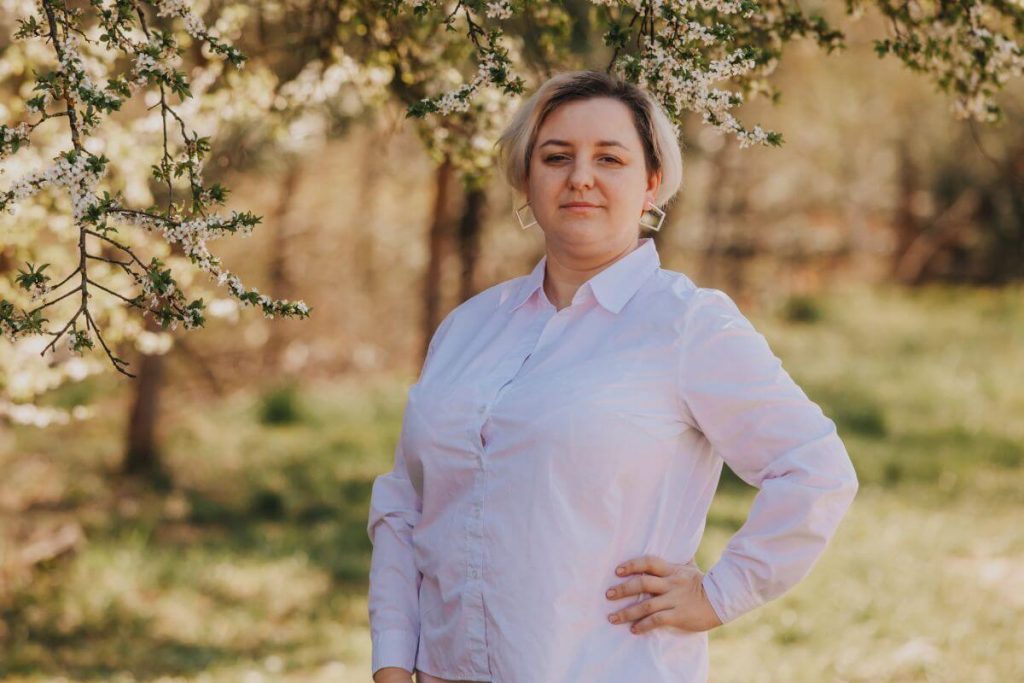 a confident woman with short hair and a button down white shirt poses in a park during the fall