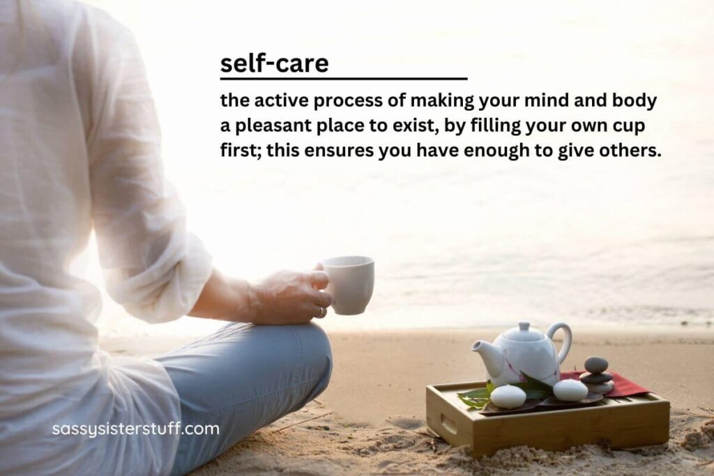 a close up a woman sitting on the beach with a mug of tea in her hand and a tray of tea supplies next to her forms a background for the definition of spiritual self care