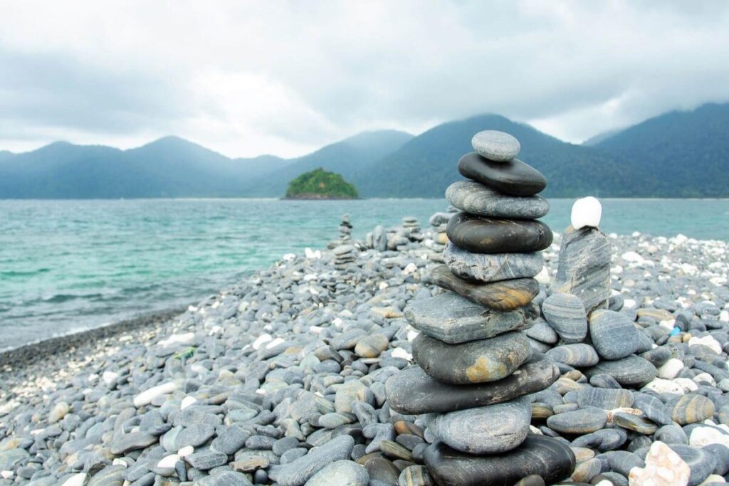 a close up of flat stones balancing on top of each other on the shoreline of a lake with mountains in the background