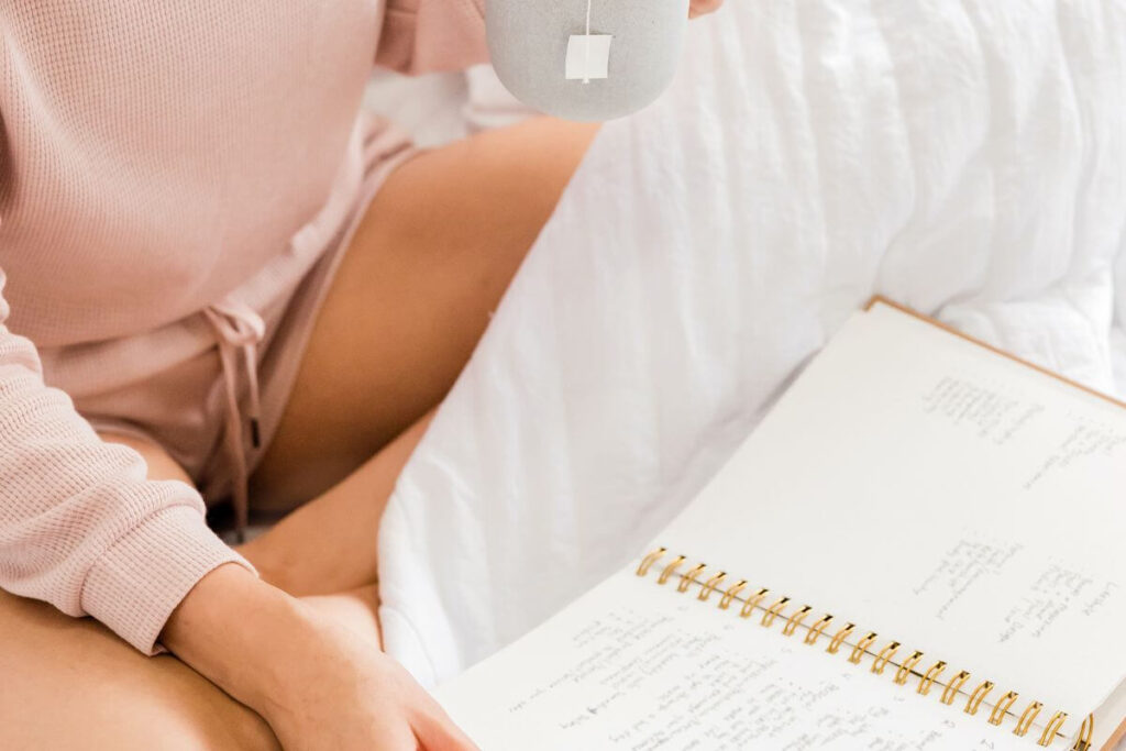 a top view of a female sitting on her bed looking at affirmations for health and wellness in her journal