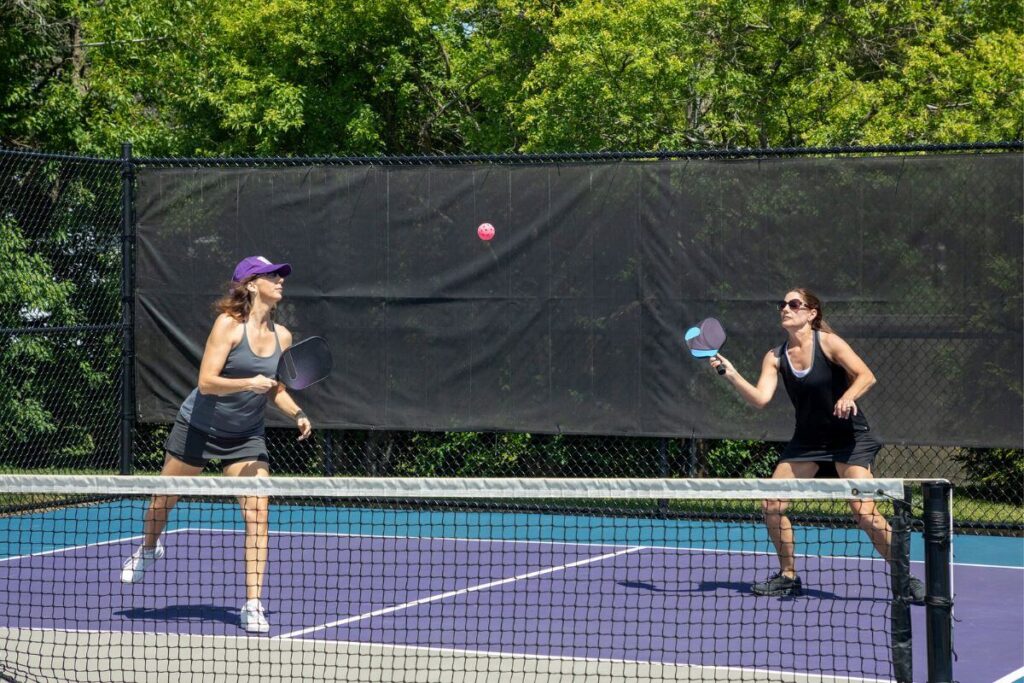 two women play pickleball on an outside court