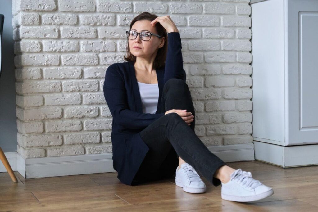 a sad middle age woman sits on her kitchen floor feeling like people are better than her