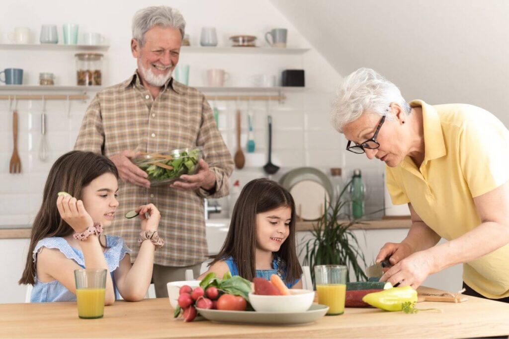 grandparents and two granddaughters enjoy preparing lunch together in their kitchen