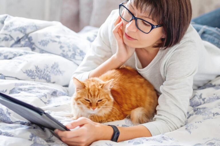 a middle aged woman studies her self care affirmations as she lays on her bed and cuddles with her orange fluffy cat