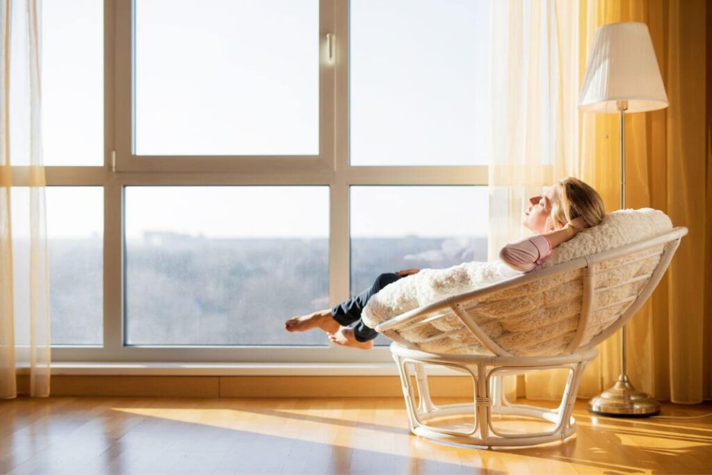 a woman peacefully relaxes in a circle chair in front of a large window because she has let go of many negative things in her life