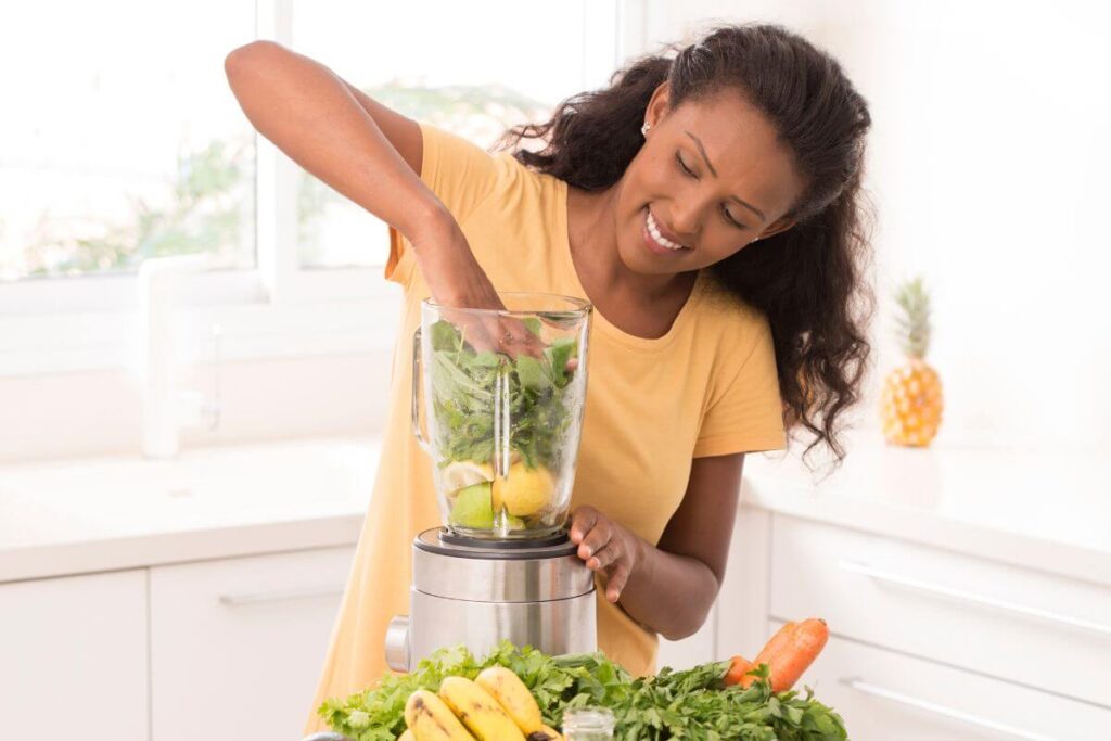 a beautiful brown skinned woman cheerfully makes a healthy morning smoothie as part of her morning routine