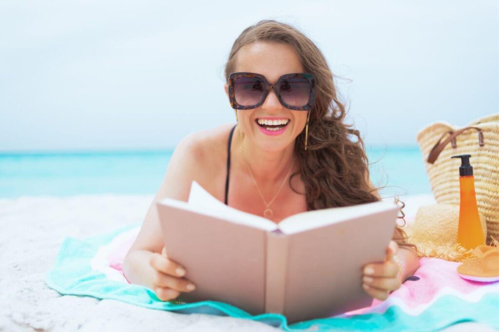 after using minimalist lifestyle tips to simplify her life, a middle aged woman lays on the beach and reads a book