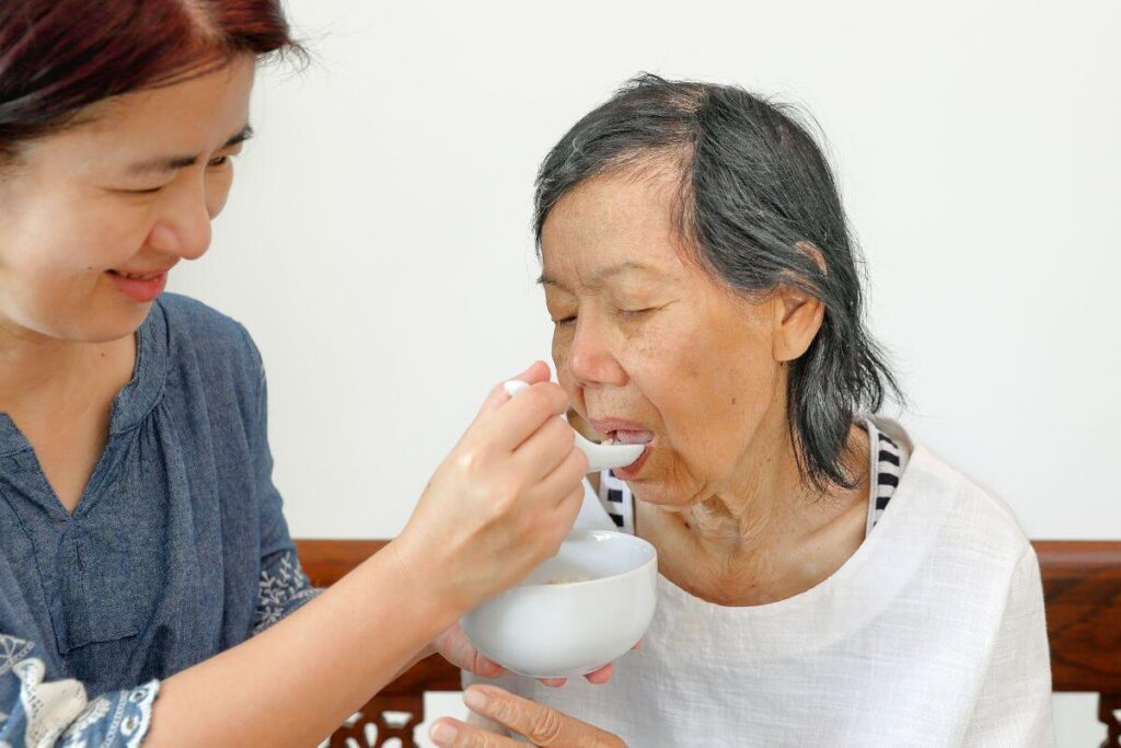 Asian woman helps her elderly mother eat soup