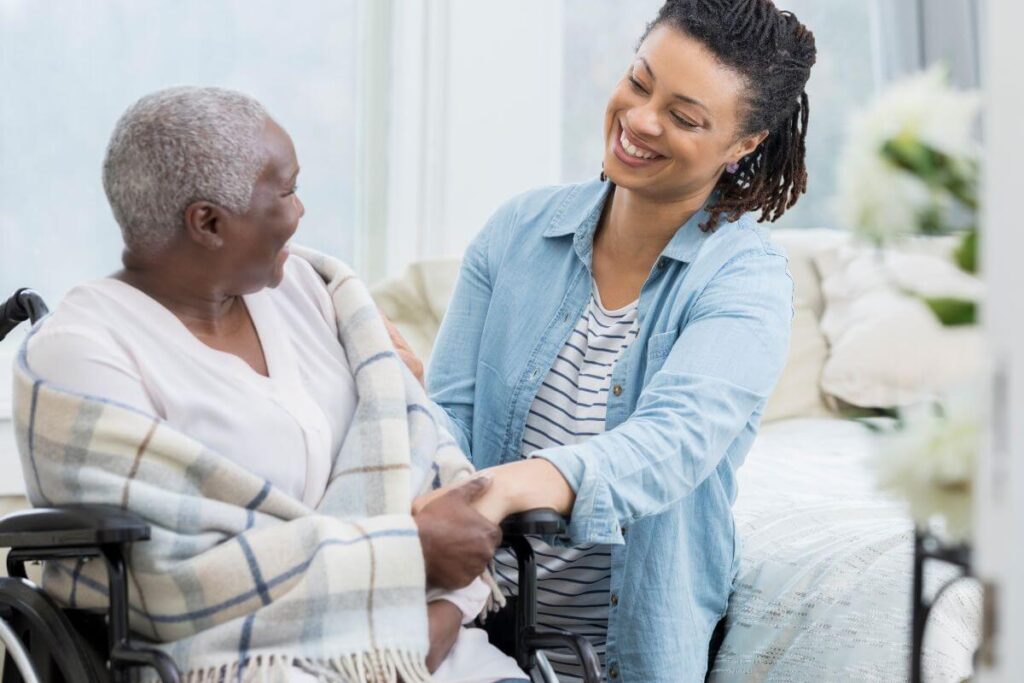 Smiling Black woman sits with an elderly woman in a wheelchair