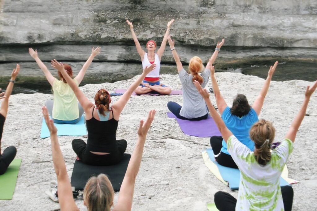 a group of ladies do yoga together on a flat rock along a river's edge