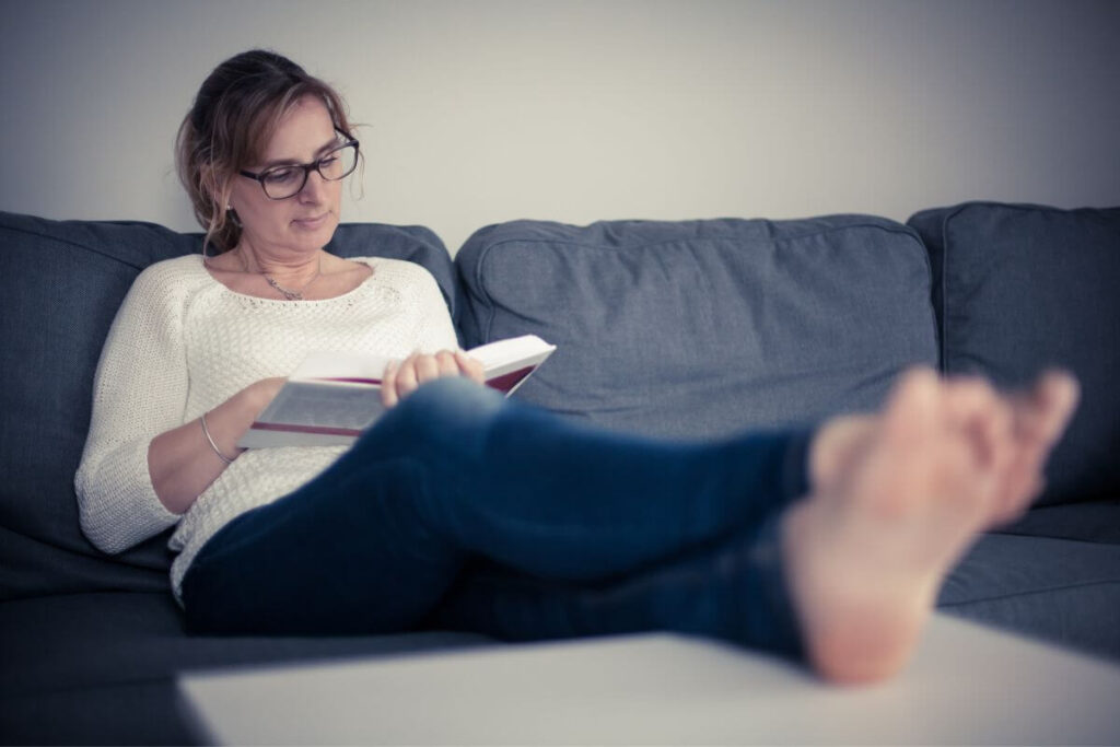 a simple middle aged woman relaxes in her living room as she enjoys reading a book