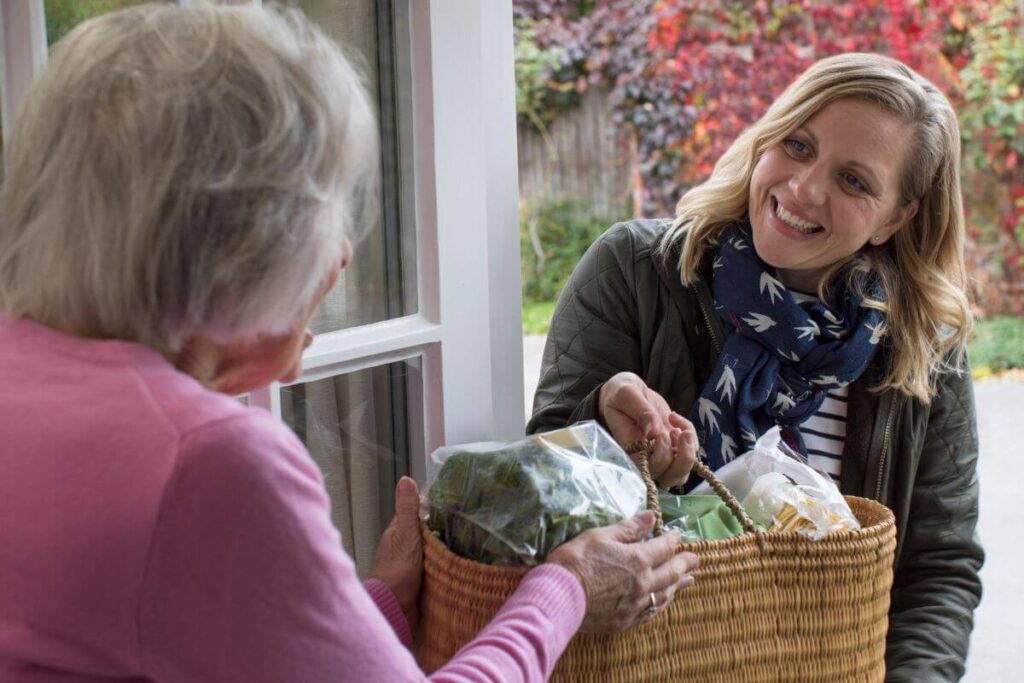 s happy middle aged women delivers a bag of groceries to an elderly woman