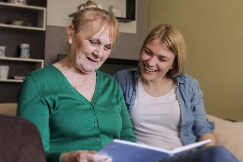 an elderly woman and an adult daughter enjoy looking at a photo album to share their memories