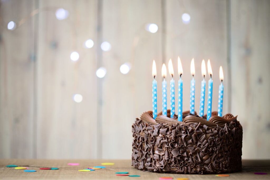 a delicious chocolate frosted birthday cake with lots of blue polka dotted candles sits on a table with confetti waiting for a big celebration of another year of life