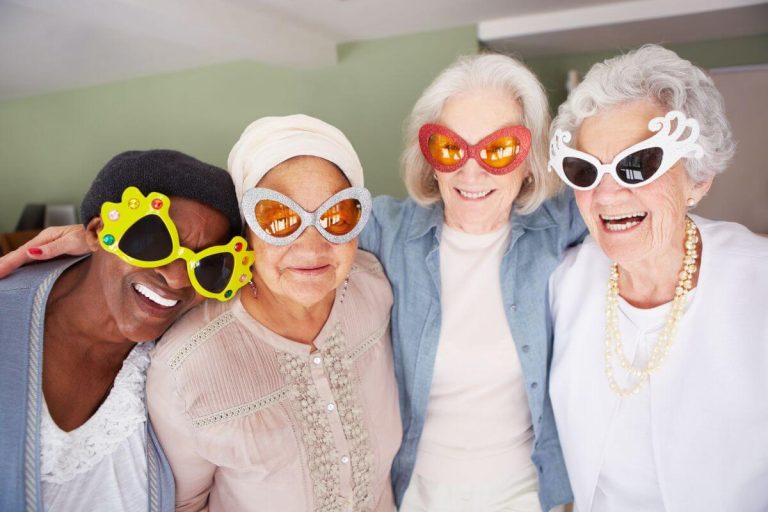 four elderly ladies laughing about wearing silly glasses and laughing about silly quotes and funny sayings about getting older