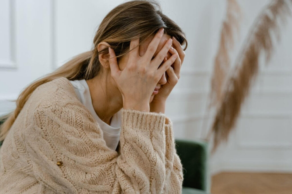 a stressed middle aged woman rests her face in her hands because she doesn't know how to make friends with social anxiety