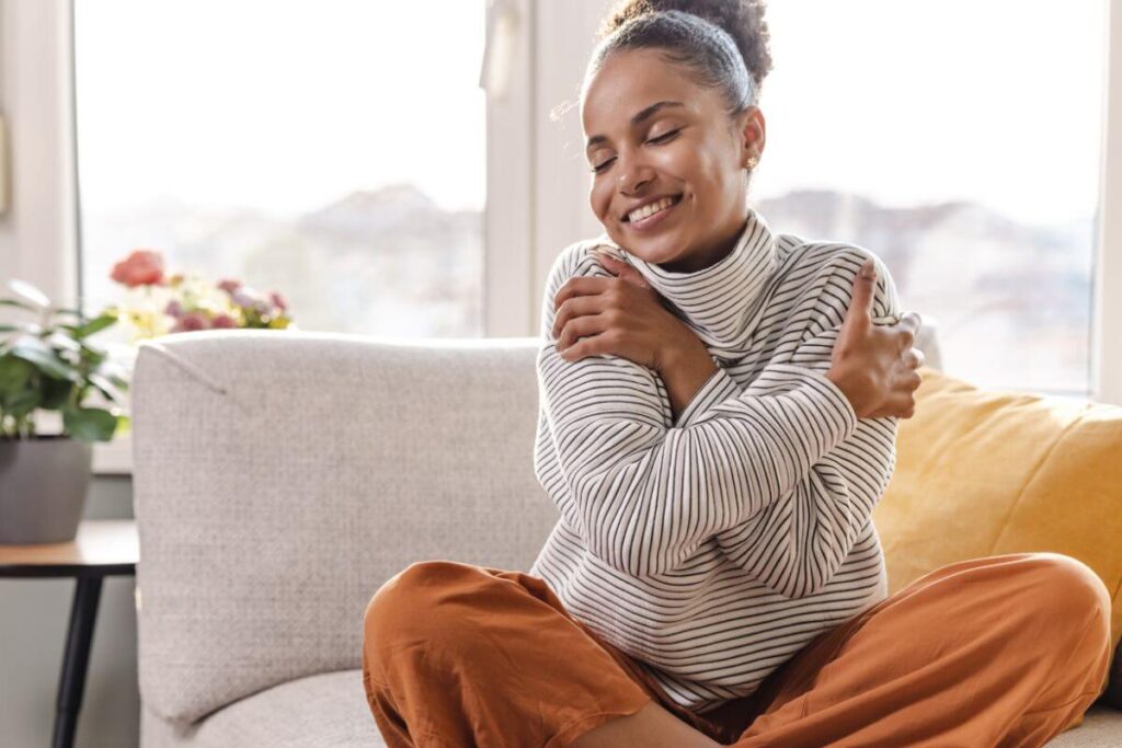 beautiful woman sitting on a comfortable chair hugging herself and showing how to start your self love journey