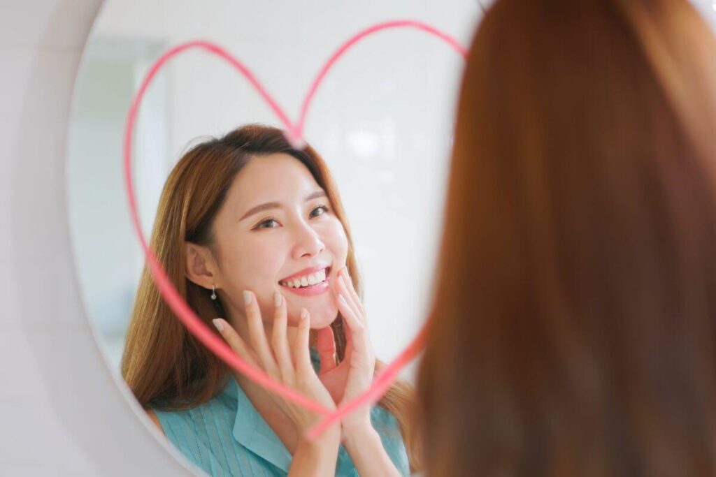 a young woman smiles in a mirror with a heart drawn on it