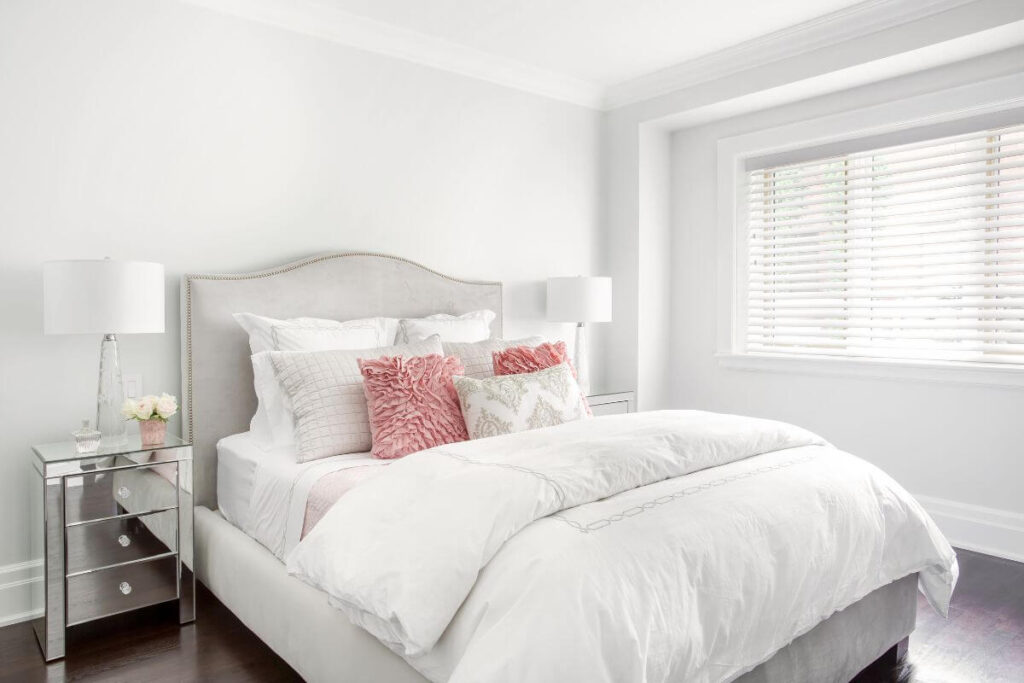 a comfortable and cozy bedroom done in white with pink accents that supports a self love journey