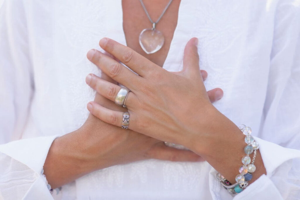 a close up of a woman with her hands crossed over her heart and a heart necklace