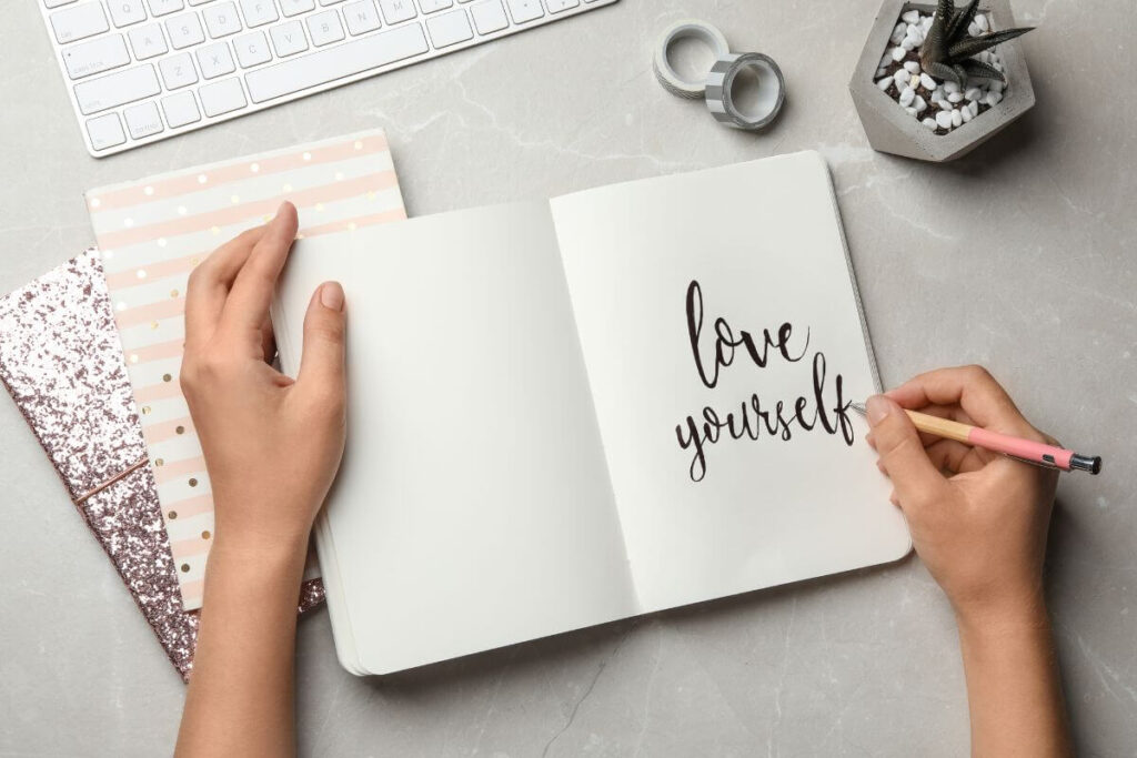 top view of a female writing love yourself in her journal