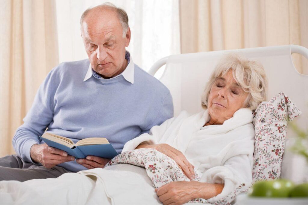 a husband reads to his sick wife while she rests in a hospice bed
