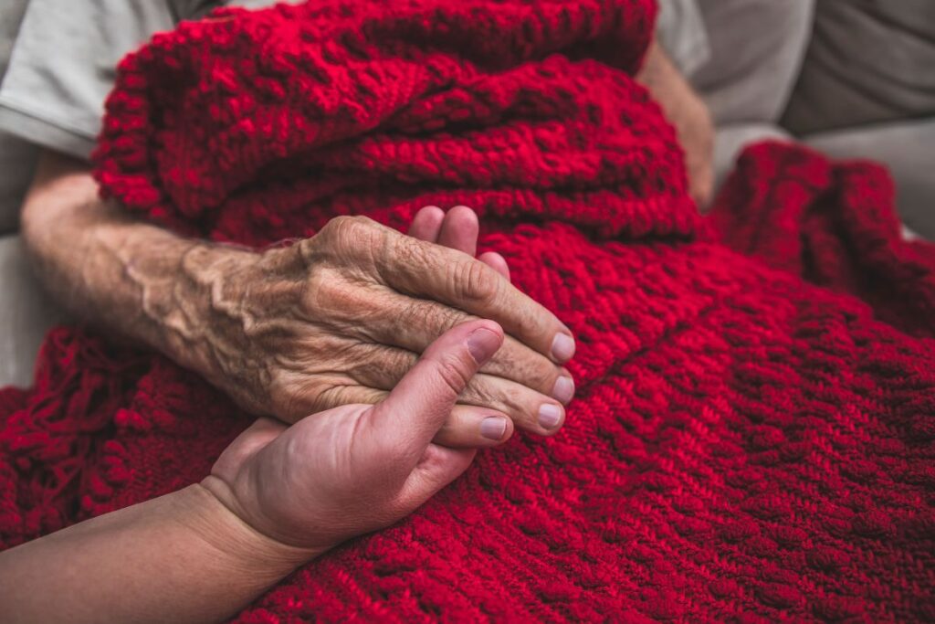 a top view of someone holding an elderly person's hand while they discuss the pros and cons of hospice care