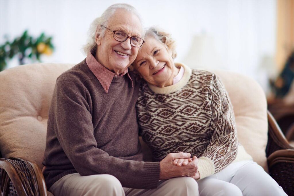 a senior citizen couple snuggle on a love seat and smile happily for the camera because their home is safe