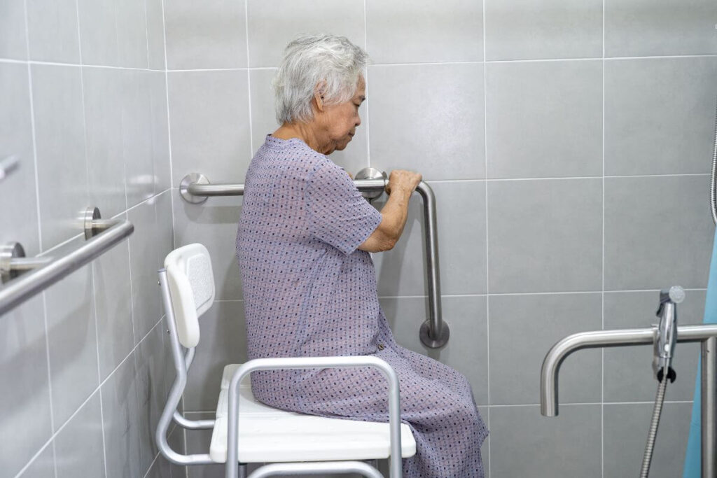 an elderly woman sits on a safe shower seat and used grab bars to maneuver in the shower