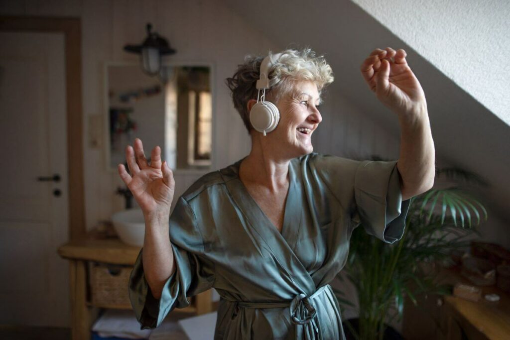 middle aged woman with headphones on happily dances to her favorite music on a self care weekend