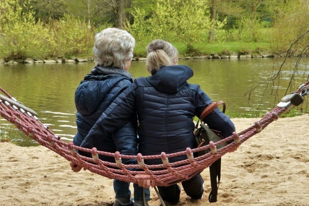 older woman with dementia is comforted by her adult daughter on a hammock by the lake
